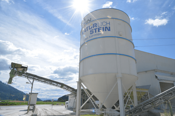Silo mit Aufschrift 'Natürlich Stein aus Kärnten' auf dem Werksgelände mit Förderband